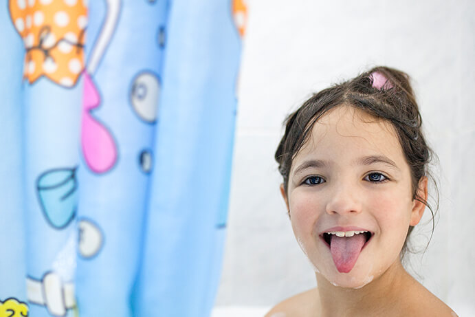 A girl in the bathtub with a cartoon shower curtain and her tongue out