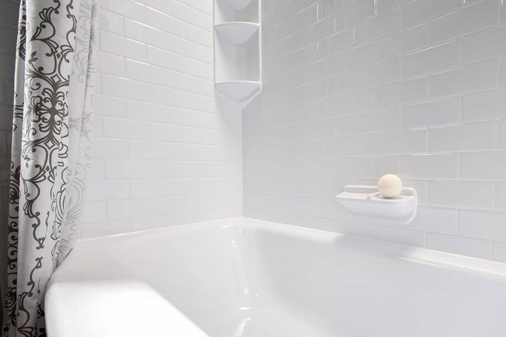 bathtub and acrylic wall pictured from the ledge of a tub with a soap holder and shelving unit visible