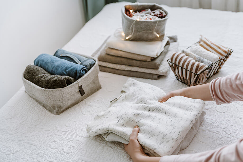 A woman is folding a stack of laundry and organizing clothes.